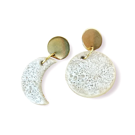 Pendientes de cerámica en forma de luna con fornituras de acero inoxidable sobre fondo neutro, diseño artesanal y estilo boho.